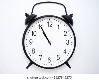 Black Retro Alarm Clock Showing 10:55 or 22:55. Classic Bell Style on White Wood Background.