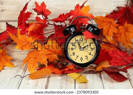 Black retro clock in autumn leaves and acorns on rustic wood for time change