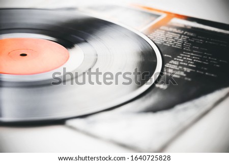 A black retro vinyl record with music recorded on it lies on the paper cover of the music album.