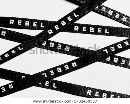 Black ribbon with white letters spelling 'Rebel', randomly criss crossing white background