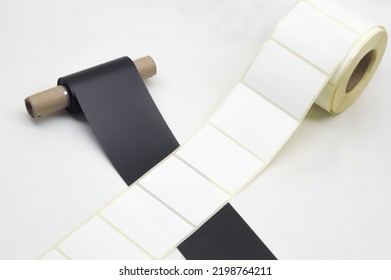 Black roll wax ribbon for thermal transfer on core and white self-adhesive label roller for a special barcode printer. Consumables and auxiliary materials for barcode printing. Selective focus - Shutterstock ID 2198764211