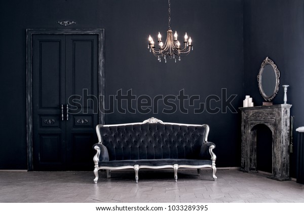 Black room in the castle with a vintage door, a\
chandelier, a sofa  and amirror and fireplace. Space where you can\
mount a person.