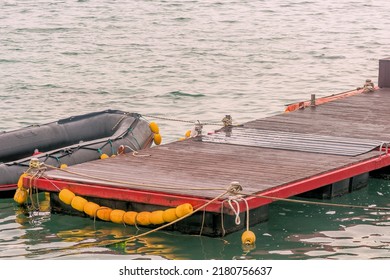 Black Rubber Dinghy Tied To Red Floating Dock.