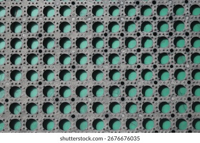 Black rubber surface with repeating round holes and green background underneath, creating geometric texture and strong color contrast