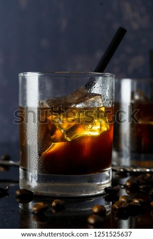 Black Russian cocktail with vodka, coffee liqueur, ice cubes in an old-fashioned glass black straw on dark background. Copy space