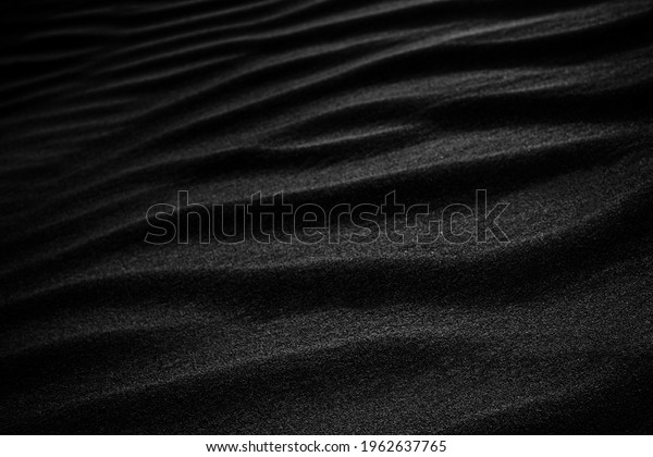 Black Sand dune. Black Sand beach\
macro photography. Background, texture, wave pattern of oceanic\
sand on the beach, black. Texture of beach sand. Black\
beach.