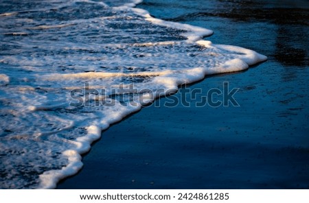 Black sandy beach with splashing water, surf, bubbles, wave foam and colorful low evening sunlight. “Anse Couleuvre“ is a remote secluded beach on tropical island Martinique. Natural background.