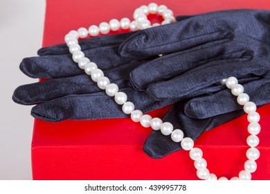 Black Satin Gloves And Pearl Beads On A Neck Decoration On A Red Background. Theater