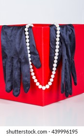 Black Satin Gloves And Pearl Beads On A Neck Decoration On The Red Background Of The Box. Theater