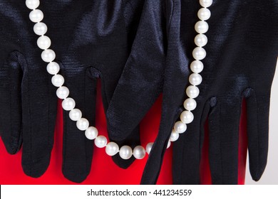 Black Satin Gloves And Pearl Beads On A Neck Decoration On A Red Background. Theater