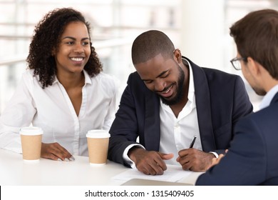Black satisfied businessman sitting with diverse partners at conference table, signing contract, make purchase and good deal, legalizing cooperation, fill document put signature on legal paper concept