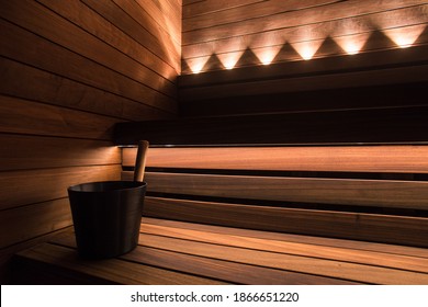 Black sauna bucket in modern design sauna with dark wood seating and LED lights.