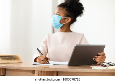 Black Schoolgirl In Surgical Mask Using Digital Tablet In Classroom, Looking Out Of Window. School Education During Pandemic. Shallow Depth