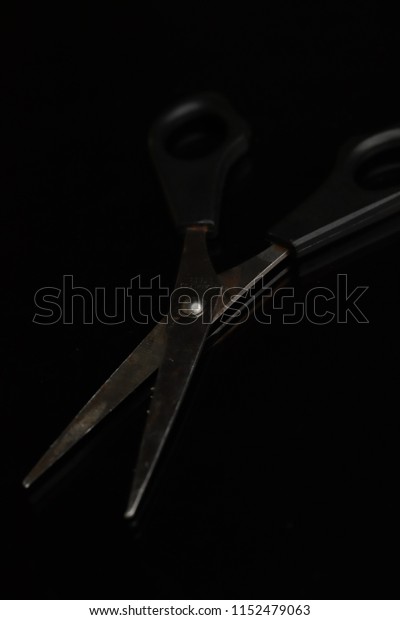 Black scissor for cutting paper hair and\
others on black background with\
reflection