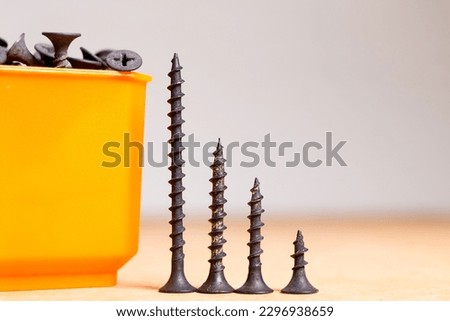 black screws on wooden surface, grouped, sorted by size and with screwdriver
