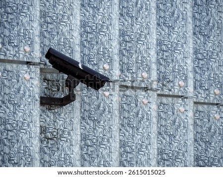 Black Security Camera Mounted on Textured Blue Wall Providing Surveillance in Urban Setting