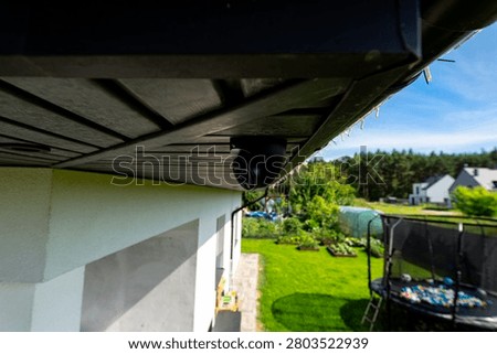 Black security dome camera observing a house backyard and surroundings from under the eaves