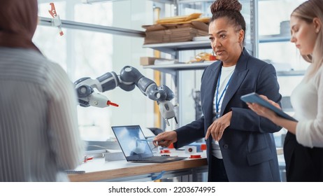 Black Senior Engineer Explaining Information To People That Look At Robot Limb. Interns Hold Devices And Discussing. Optimisation Of Autonomous Manufacturing Facility That Creates High Tech Products.