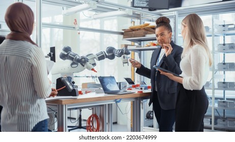 Black Senior Engineer Explaining Information. People Look At Robot Limb. Interns Hold Devices And Discussing. Optimisation Of Autonomous Manufacturing Facility That Creates High Tech Products.