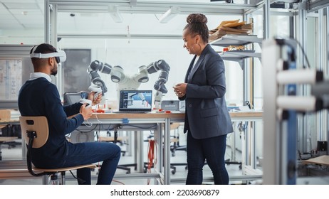 Black Senior Engineer Talks to Young Male Computer Scientist Who is Wearing Virtual Reality Headset and Uses Controllers to Remotely Manipulate Robotic Hand. High Tech Research Laboratory Concept - Powered by Shutterstock