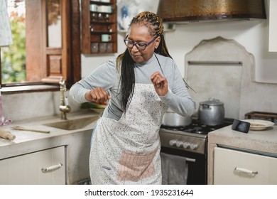 Black Senior Woman Having Fun Cooking And Dancing Inside Vintage Kitchen