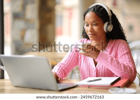 Black serious student studying using laptop and headpone in a bar terrace