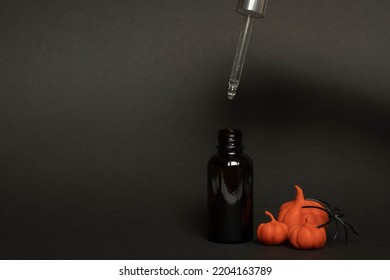 A Black Serum Bottle On A Black Background With Plasticine Pumpkins And A Spider , A Creative Halloween Concept