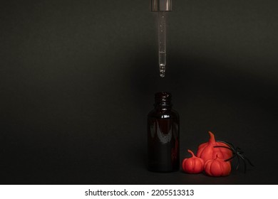 A Black Serum Bottle On A Black Background With Plasticine Pumpkins And A Spider , A Creative Halloween Concept