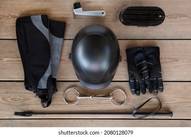 Black set of equipment for horse care and riding: helmet, whip, gloves, bridle, brushes on the wooden background