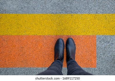 Black Shoes Standing On The Asphalt Concrete Floor With Yellow And Orange Lines. Feet Shoes Walking In Outdoor. Youth Selphie Modern Hipster