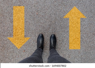 Black Shoes Standing On The Asphalt Concrete Floor With Two Yellow Arrows. Feet Shoes Walking In Outdoor. Youth Selphie Hipster