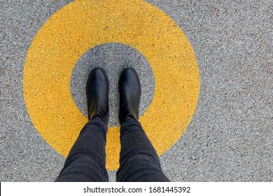 Black shoes standing in yellow circle on the asphalt concrete floor. Comfort zone or frame concept. Feet standing inside comfort zone circle