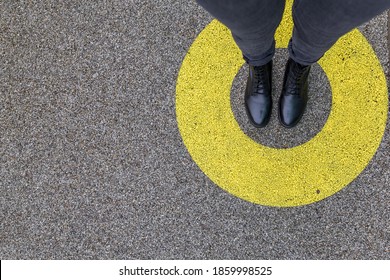 Black shoes standing in yellow circle on the asphalt concrete floor. Comfort zone or frame concept. Feet standing inside comfort zone circle. Place for text, banner