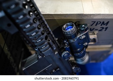 Black Shooting Scope Optics Mounted On Metal Bar Displayed At Weapons Exhibition Fair, Closeup Detail To Blue Lens