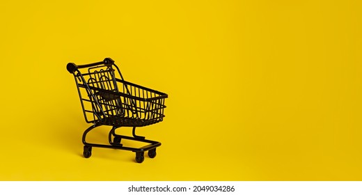 Black Shopping Cart Isolated On A Vibrant Yellow Background. Creative Black Friday Concept. Sale Or Promotion Banner. Minimal Retail Store Idea.