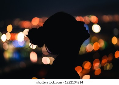 Black Silhouette Of Beautiful Girl With Messy Hair Bun With City Lights In The Backround Looking Up The Sky, Thoughtful Watching The View