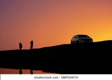 Black Silhouette Of Couple Adult Pair Which Take Photo.  Family Adult Couple Meet Bright Sunrise Or Sunset At Sea Coast Or Lake Or River 