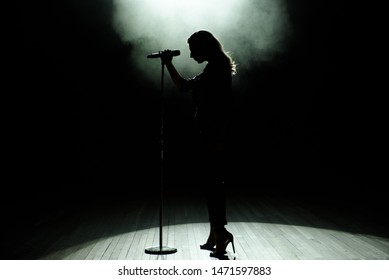 Black Silhouette Of Female Singer With White Spotlights In The Background.