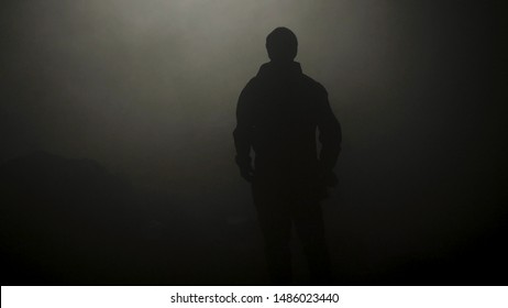 Black silhouette of man standing in smoky dark. Stock footage. Mysterious silhouette of young man stands in darkness lit only by dim light in haze - Powered by Shutterstock