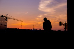 Black Silhouette Of A Man That Is Looking Down In Front Of The Orange Sunrise With A Blue Sky In The City