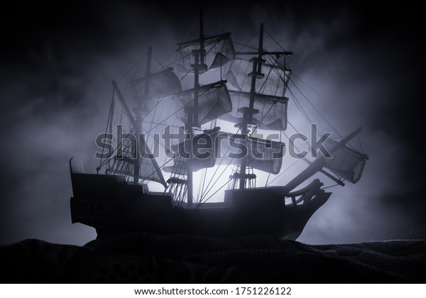 Black silhouette of the pirate ship in night. night\
scene of ghost pirate ship in the sea with mysterious light.\
Selective focus