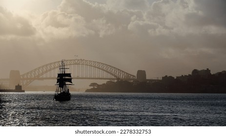 Black silhouette of a traditional barquentine or schooner barque tall ship cruising westwards the waters of Port Jackson in a very hazy afternoon-Harbour Bridge in the background. Sydney-NSW-Australia - Powered by Shutterstock