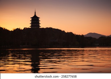 Black silhouette of traditional Chinese pagoda on orange evening sky background. Coast of West Lake. Famous park in Hangzhou city center, China