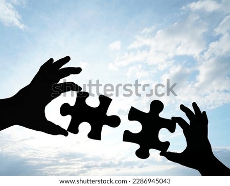 black Silhouette of two hand holding couple of jigsaw puzzle piece on blue sky with clouds background. connection idea, sign, symbol, concept. 