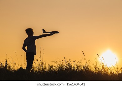 Black Silhouette Of Young White Kid Holding Toy Plastic Blue Plane In Hand. Confident Boy Setting Big Goals Concept. Horizontal Color Photography.