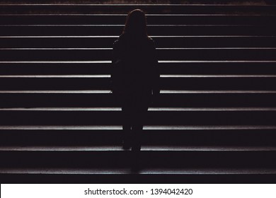 Black silhouette of a young woman casually dressed climbing up the city street stairs – Single person walking in the dark of the night – Concept image for leadership, achievement or independence - Powered by Shutterstock