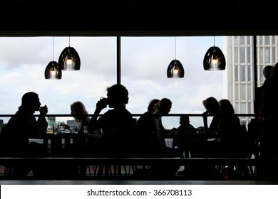 Black Silhouettes Of People Having Lunch Inside A Modern Restaurant With Big Windows