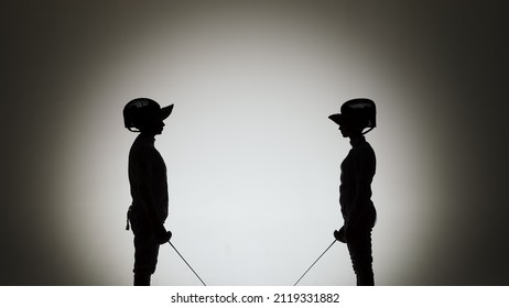 Black silhouettes of two female swordsmen fighting a duel. Athletes cross rapiers and deliver attacking blows. The girls pose in a dark studio on a white background in a spotlight spot. Slow motion. - Powered by Shutterstock