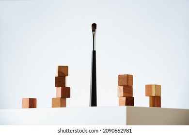 black and silver makeup brush standing up and wooden cedar cubes on white podium and background. Eco friendly beauty and self-care with recycled materials. Hero shot