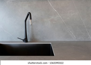 A black sink and a matt-finish black faucet set against grey surfaces made of porcelain slabs that mimic the look of natural stones. 